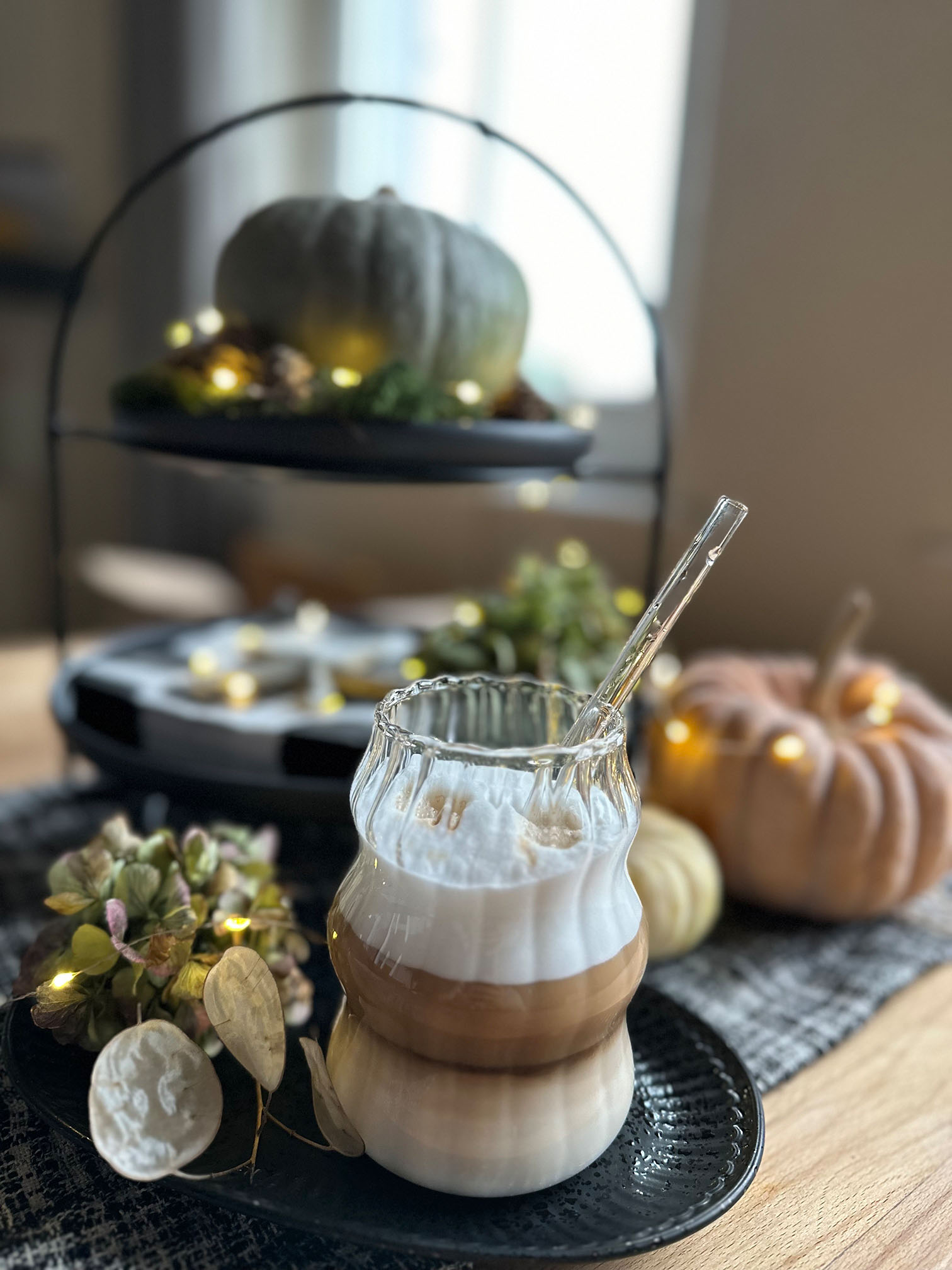 Ein geschichteter Latte im Glas vor herbstlicher Deko mit Kürbissen und Lichtern