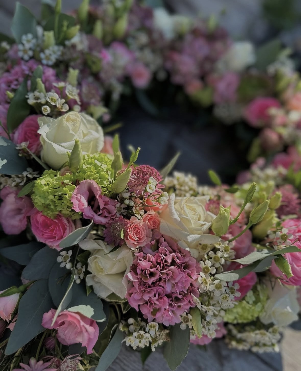 Ein bunter Blumenkranz mit weißen Rosen, pinken Blüten und grünen Blättern