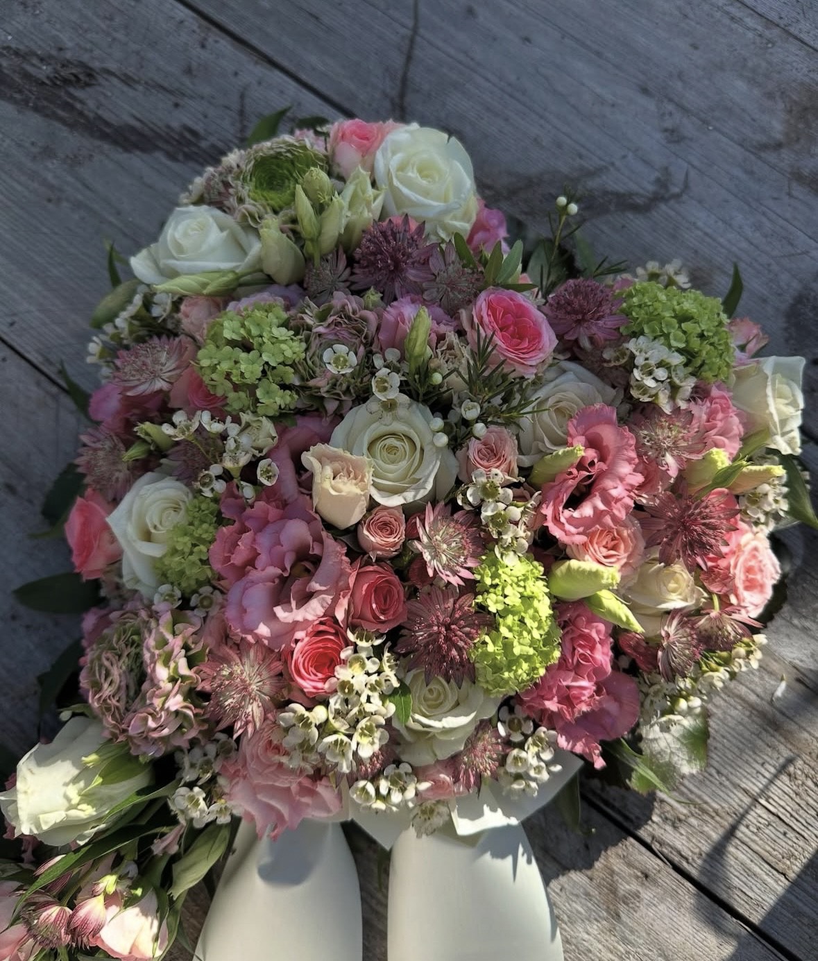 Ein bunter Blumenstrauß mit weißen und rosa Rosen liegt auf Holz neben weißen Schuhen