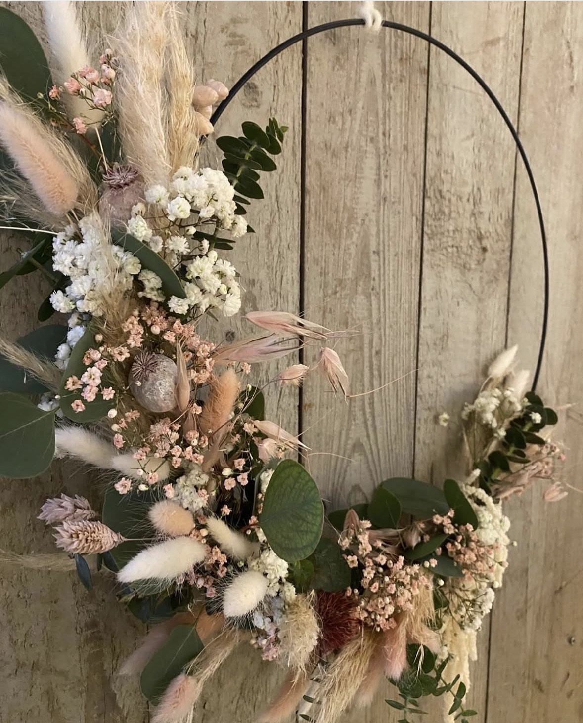 Ein zarter Kranz aus Trockenblumen in Pastelltönen an einer Holzwand hängend