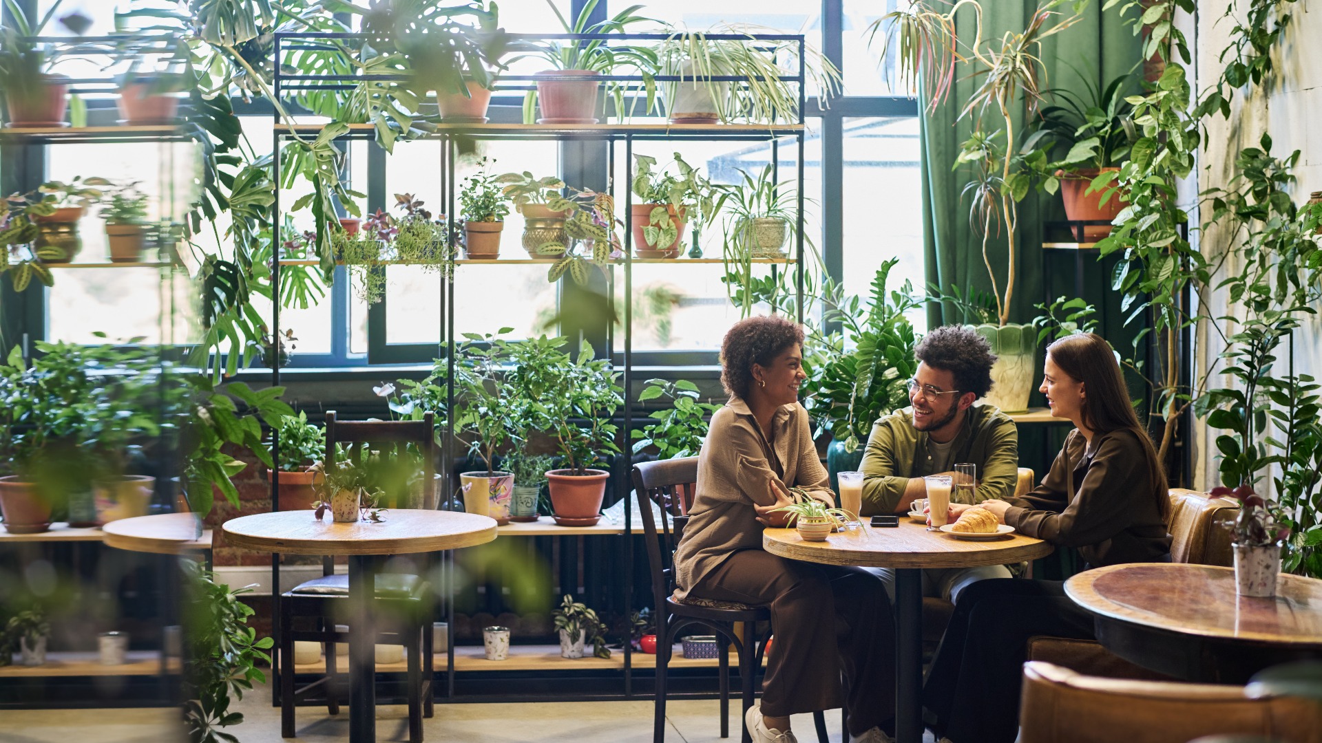 Eine Gruppe von Freunden sitzt an einem Tisch in der Ecke eines Cafés mit Grünpflanzen.